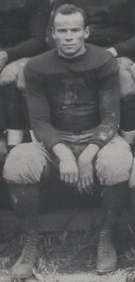 Posed photograph of Wray seated and wearing a football uniform bearing a "F" on the chest with pads but no helmet