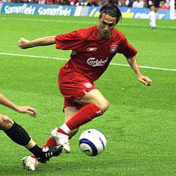 A coloured photograph of a man controlling a football. He is dressed in a red kit.