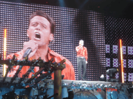 A man wearing a red shirt and singing on stage.