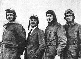 Four men, each wearing a flying helmet and goggles