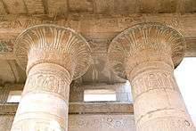 Two stone columns supporting a roof, painted with faded colors and incised with writing of Egyptian hieroglyphs