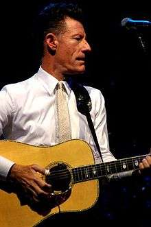 An older man holding a guitar and looking to his left.