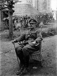 A black and white photograph of a man wearing military uniform seated on a garden chair on a lawn