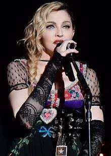 A closeup photo of Madonna with shoulder-length wavy blonde hair, heavy makeup and a colorful, low-cut blouse