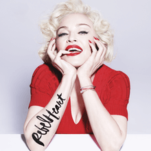 Madonna in a red dress with her hands on her face, rested on a desk. The album's name is visible on her right arm