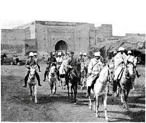 A photograph of General Mangin entering Marrakesh through a large gate at the head of a column of French horsemen