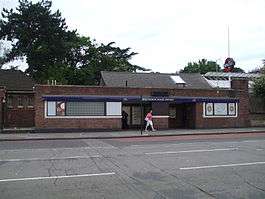 A red-bricked building with a rectangular, dark blue sign reading "MANOR HOUSE STATION" in white letters all under a light blue sky with white clouds