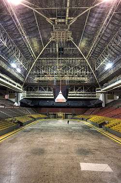 The interior of an arena. There are bands of seats of different colours, and there is a high, vaulted ceiling.