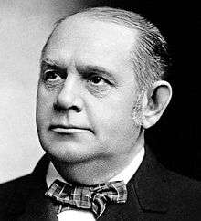 A closely cropped portrait photograph of a man about fifty, balding, looking up and to the viewer's left (his right). He wears a bow tie, which is about as far down as the viewer can see.