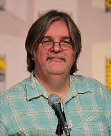 A man in glasses and a plaid shirt sits in front of a microphone.