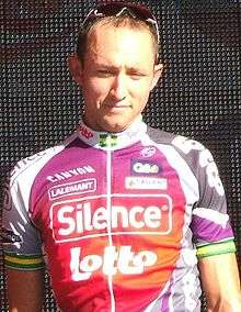 A man in his mid-twenties wearing a red, purple, and white cycling jersey, with green and gold arm bands.