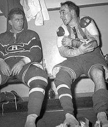 Richard, in full uniform except for his skates, sits on a locker room bench and stares at teammate Toe Blake beside him