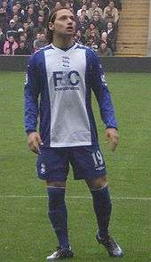 Dark-haired young man wearing blue and white football kit.