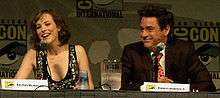Rachel McAdams and Robert Downey Jr. sitting at the farside of a table behind two microphones.