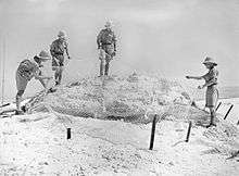 Four soldiers standing around an obscured gun position.