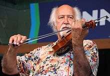 Michael Doucet playing the fiddle with the bow in his right hand. He has white hair.