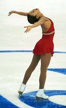 A female ice skater in white boots and a red dress