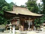 A small wooden building with a roofed, raised veranda with a handrail