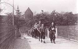 Ragtag group of men with guns marching away from a walled fortress