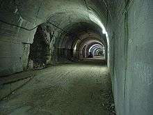 A long view down a lit gravel—paved concrete tunnel which has a series of openings on the left-hand side