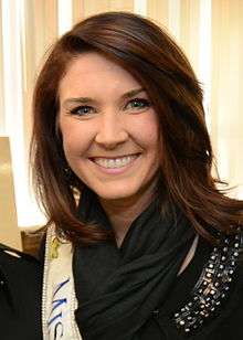 A brown-haired smiling woman wearing a black scarf and a white Miss Oregon sash over a black top