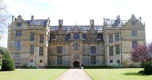 Facade of house built of yellow stone. Three floors with large, mullioned windows and Dutch gables to the roof.