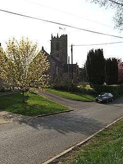 Stone building with square tower. In the foreground is a road.