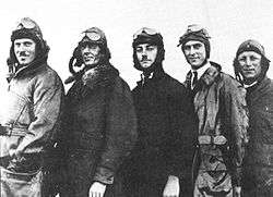 Informal three-quarter portrait of five men in flying suits and goggles