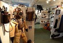 Interior view of a museum display showing standard diving dress with copper helmet in the foreground.
