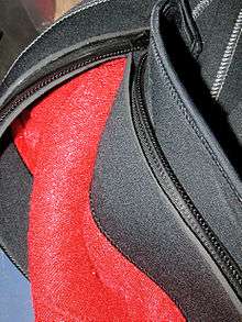Detail of the zipper of a semi-dry wetsuit, showing one end of an open zipper and the neoprene flaps that cover it on the inside and outside of the suit to protect the zipper, improve comfort, and reduce leakage through the closed zip.