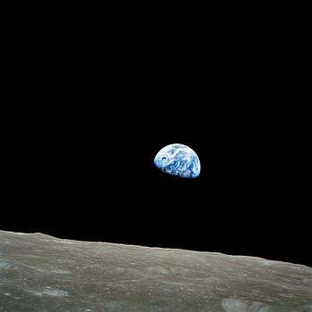 The small blue-white semicircle of Earth, almost glowing with color in the blackness of space, rising over the limb of the desolate, cratered surface of the Moon.