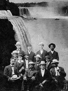 A dozen African American men seated with Niagara Falls in the background