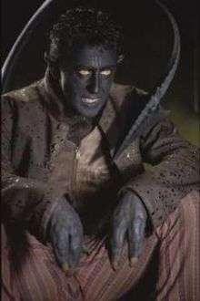 Close up of a sitting man with hands like claws, a long, pointed tail, pointed ears, and an intimidating, ghoulish expression on his face.