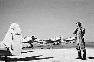 Pilot in flying suit standing by four single-engined military monoplanes