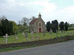 Small stone building with gravestones in the foreground.
