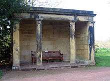 A stone loggia with four columns supporting an entablature, and containing a wooden seat