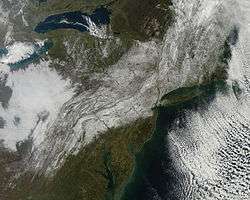 A satellite image of the northeastern United State. A swath of snow covers the ground from the Appalachians in western Virginia through Pennsylvania, northern and central New Jersey, the New York City metropolitan area and Hudson Valley into New England. There are patches of cloud on either side.