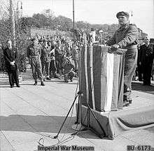 Man standing at podium with a crowd behind