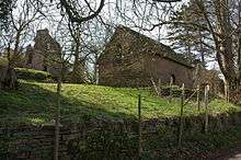 On a bank, tucked behind trees is a simple chapel, to the left of which are castle ruins