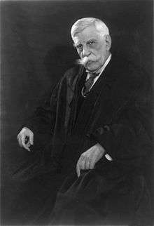 Man in shirt and tie and judge's robes seated in a chair