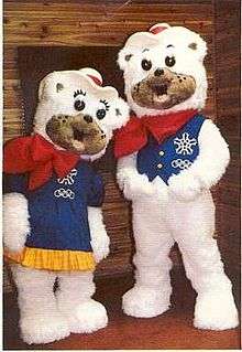 Two polar bear mascots with fuzzy white fur. The female is wearing a blue dress, the male a blue vest. They each wear a red bandana and cowboy hat.
