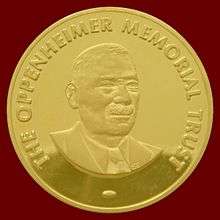 A golden medallion with an embossed image of a mustached man. Surrounding the bust in bold uppercase type is embossed the words, THE OPPENHEIMER MEMORIAL TRUST.