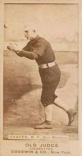 A man in a baseball uniform has his arm out in front of body attempting to catch a baseball.