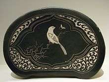 An oval shaped pottery pillow with flat sides. It has an image of a white bird sitting on a branch.