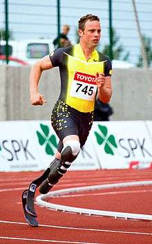 A man in a spandex singlet runs on a track.  He has two prosthetics below the knees