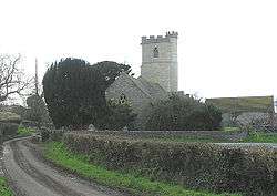 Stone building with prominent square tower. In the foreground is a road and wall.