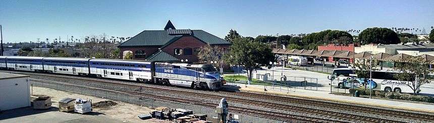 Northbound Surfliner pulling into station where a regional bus is parked and a local bus boards passengers at the covered island platform