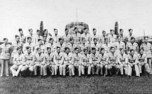 Military personnel standing or seated in front of twin-engined military monoplane
