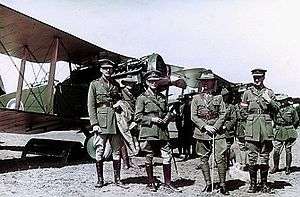 Row of biplanes with four men in military uniforms in the foreground