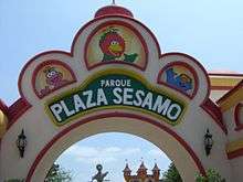 A view of upper part of a sign, mostly white, with pictures of three characters above the words "Parque Plaza Sesamo" in large, white letters.